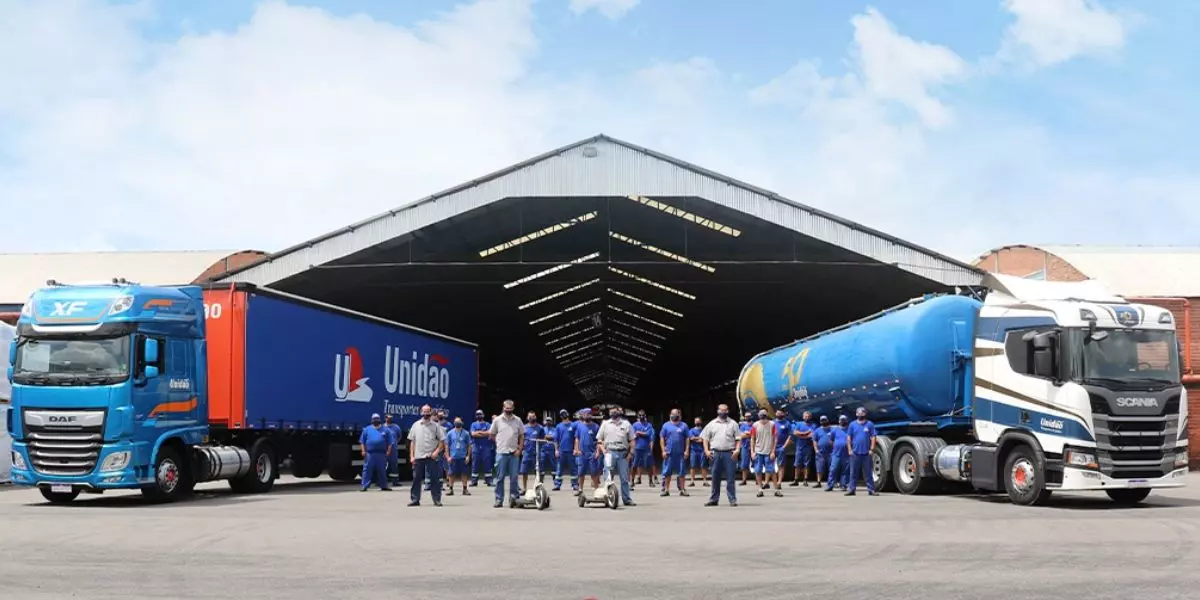 A foto mostra duas carretas e uma equipe de motoristas da Unidão Transportes