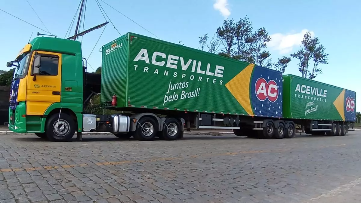 A foto mostra uma carreta bitrem verde e amarela da Aceville Transportes