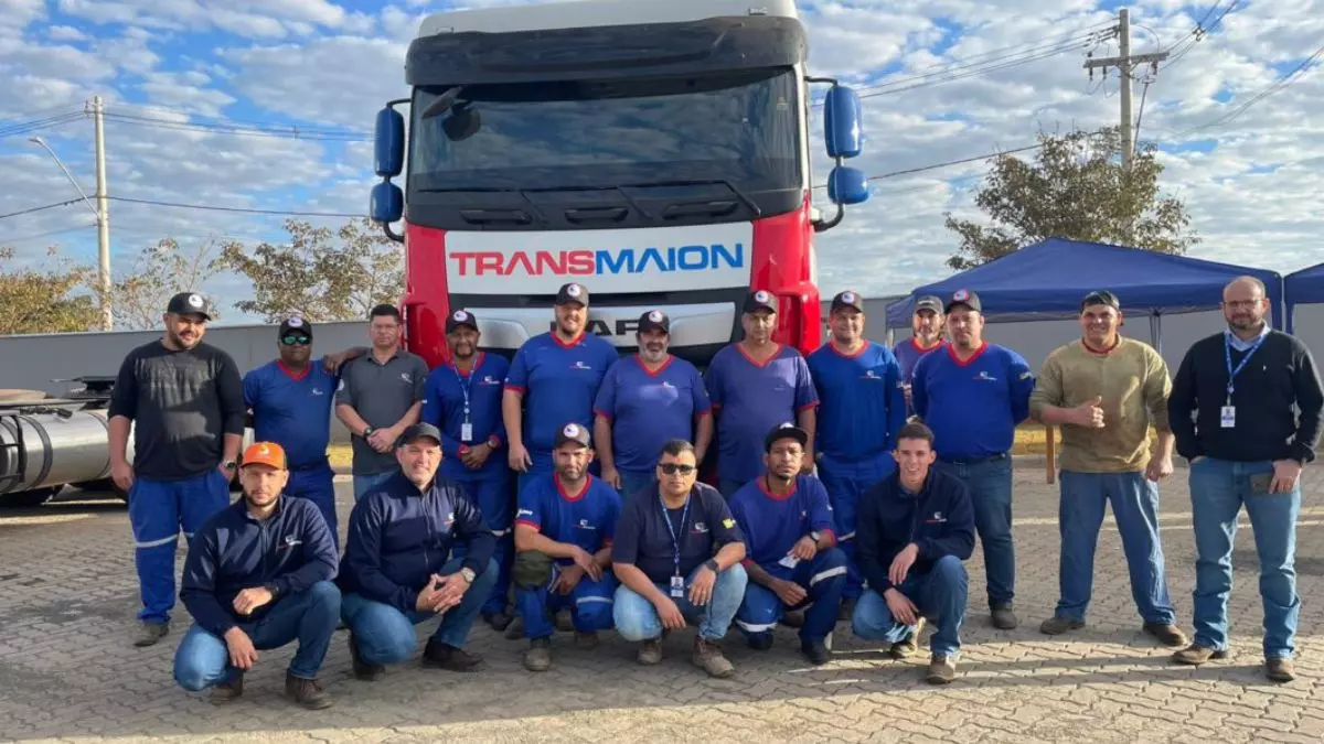 A foto mostra um caminhão da Transmaion e vários motoristas